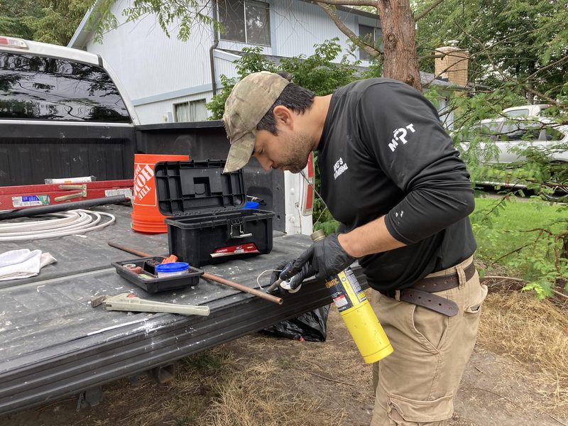 A plumber in a Mike's Plumbing shirt soldering copper pipe at a truck tailgate